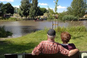 2 Senioren sitzen auf einer Bank in einem Park mit großem See.